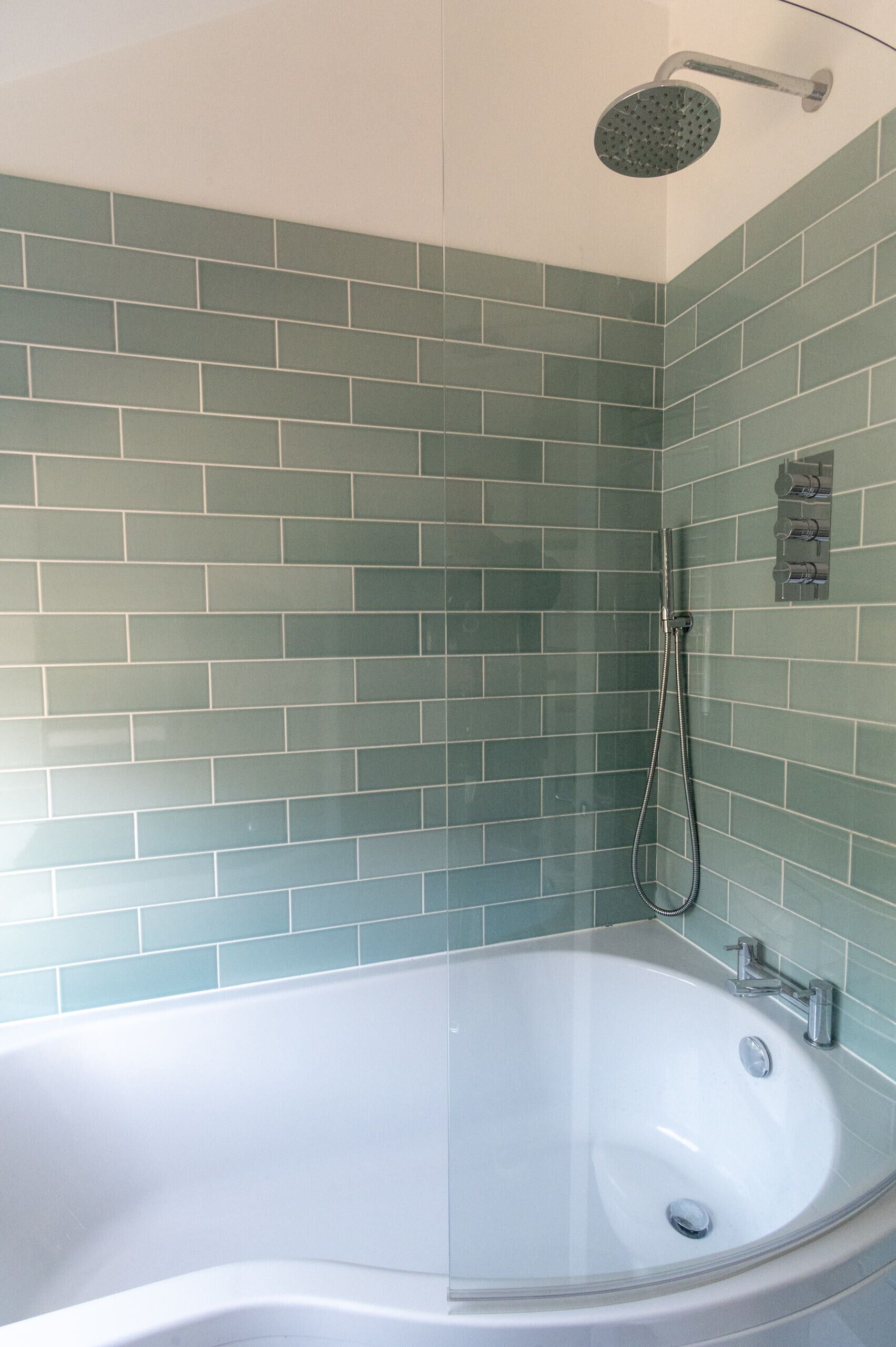 Een badkamer met een bad, douche en groene tegels.