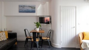 Ein modernes Wohnzimmer mit Sofa, Esstisch mit Stühlen, einer Topfpflanze, einem Flachbildfernseher und einer Tür.