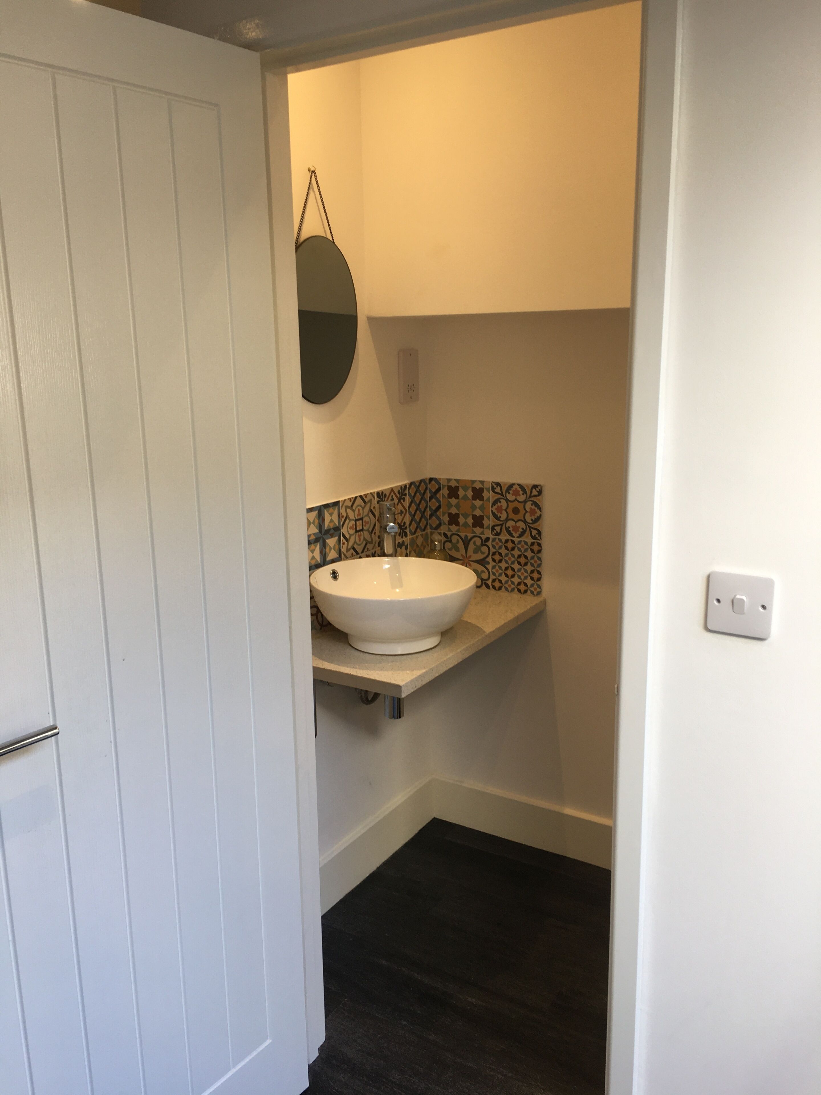 A bathroom with a white sink, a mirror, patterned tiles, and dark flooring.