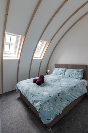 Ein Schlafzimmer mit gewölbter Decke, einem Bett mit floralem Bettbezug und zwei Oberlichtern.
