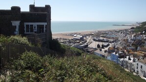 Eine Küstenstadt mit einem markanten Steinhaus, einem Strand und einem Pier in der Ferne.