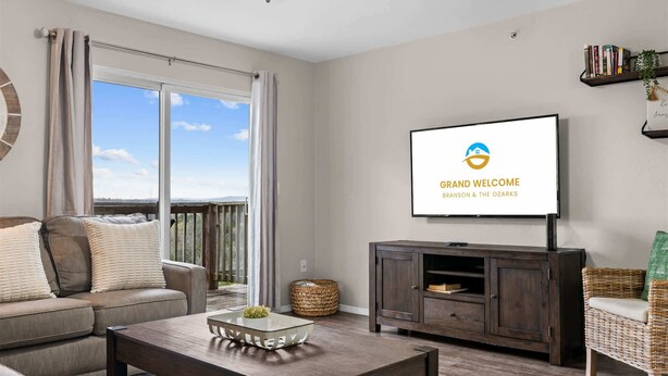 Een woonkamer met een bank, een salontafel, een aan de muur bevestigde televisie en een balkon met uitzicht.