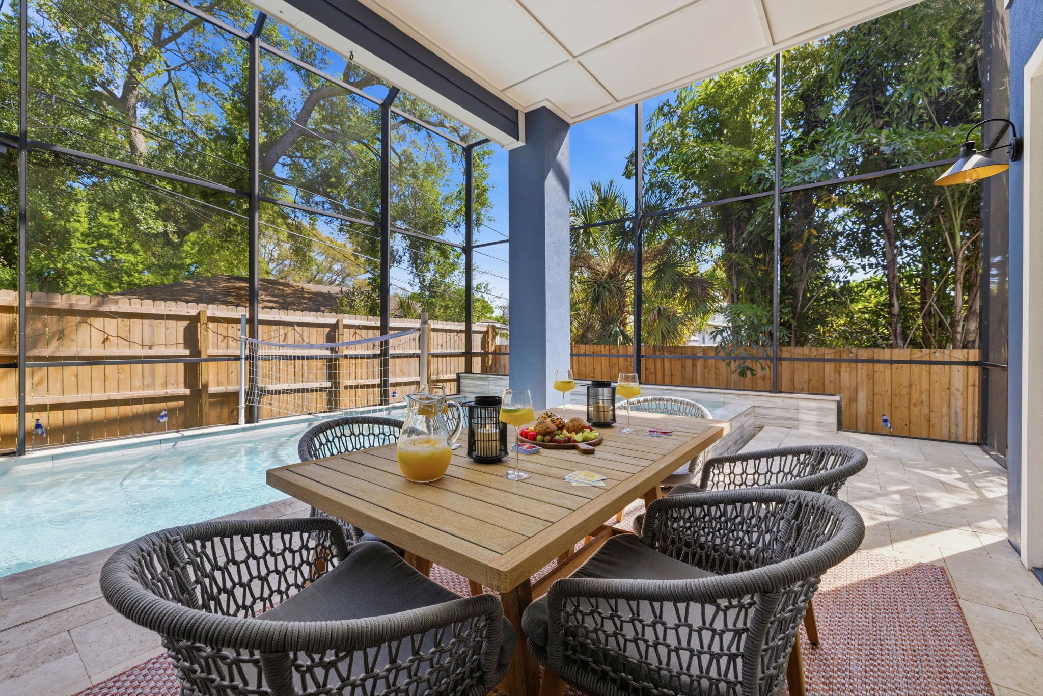 Un patio al aire libre con piscina, sillas de mimbre, una mesa de madera y una cerca de madera al fondo.