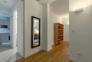 A hallway with a wooden bookshelf, a framed mirror, and a kitchen area visible through an open door. - Luxury 4-Bedroom Cibeles Exclusive Apartment in the Heart of Madrid (Madrid)