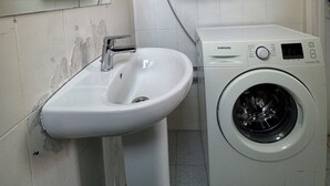 Kylpyhuone, jossa on pesuallas, peili, pesukone ja laatoitetut seinät.