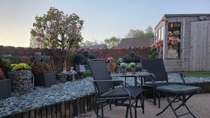 A patio area with outdoor furniture, a garden with various plants and decorations, and a wooden shed.