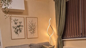 A living room with a grey sofa, a wooden side table with a candle and a vase, and framed botanical prints on the wall.