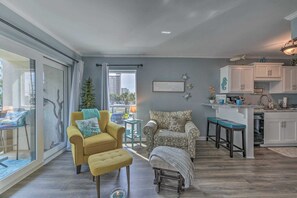 Ein modernes Wohnzimmer mit einem gelben Sessel, einem gemusterten Sessel und einem kleinen Ottomanen. Eine Glastür führt auf einen Balkon mit Blick auf die Stadt.