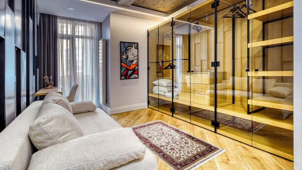 Ein modernes Hotelzimmer mit einer Couch, einer Glastrennwand, einem Holzschrank und einem Bild an der Wand.