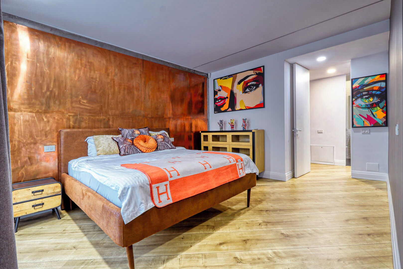 A modern bedroom with a wooden headboard, a bed with a striped bedspread, a wooden nightstand, and a dresser.
