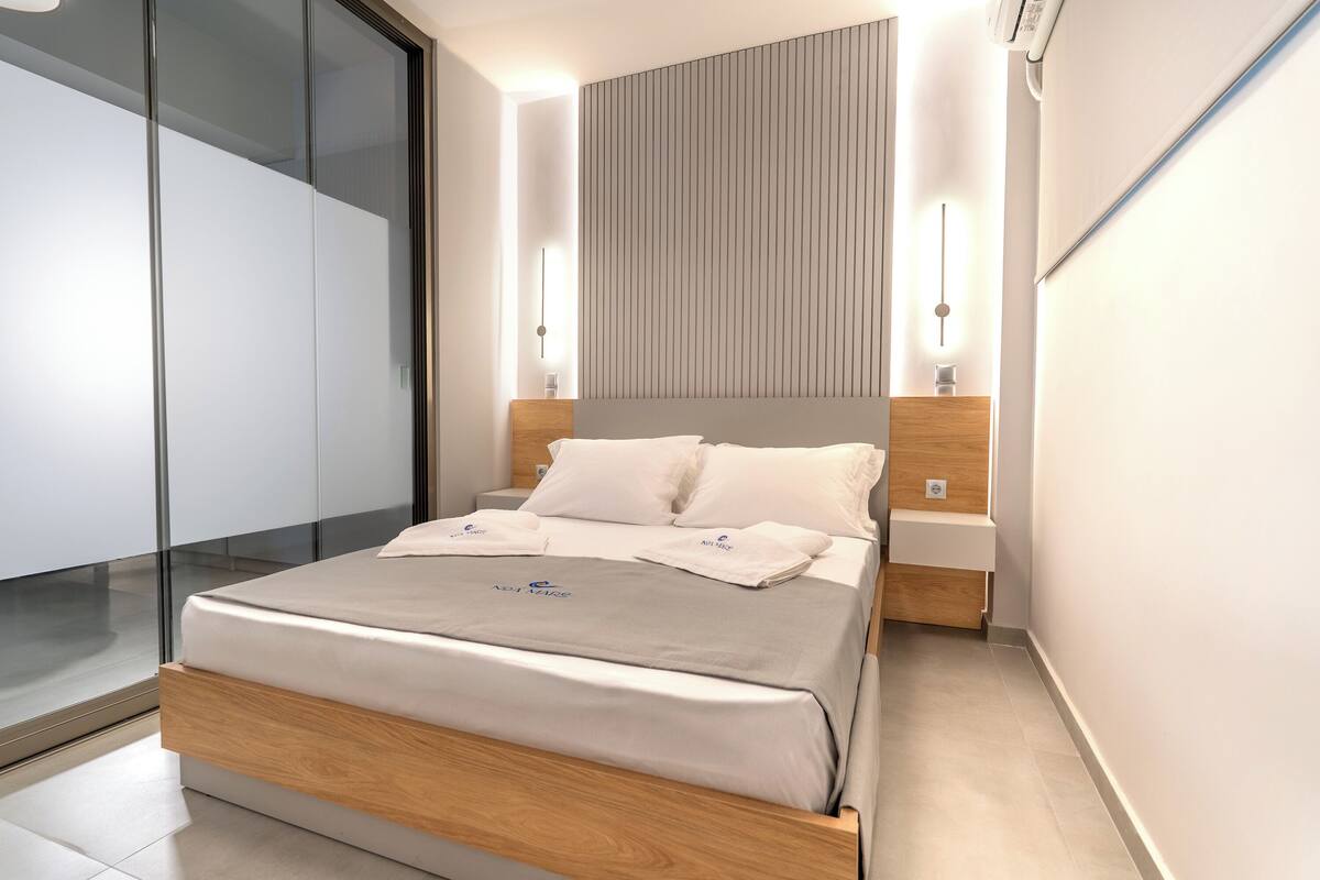 Une chambre moderne avec un lit, des tables de chevet et une vue à travers une porte vitrée.
