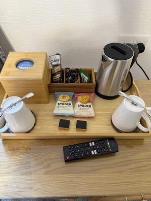 A wooden tray with a coffee maker, two mugs, a keyboard, and snack packets.