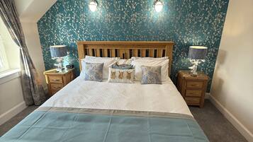 A bedroom with a wooden bed, floral wallpaper, two bedside lamps, and a window with curtains.