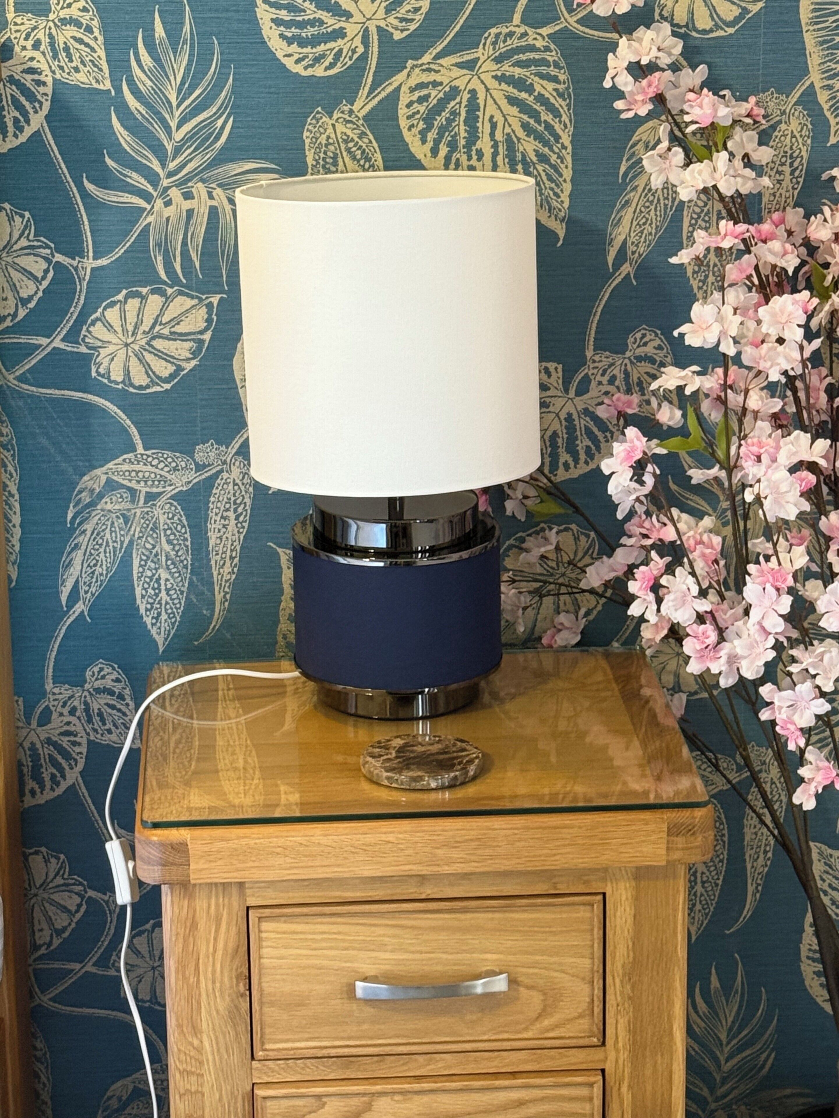 A bedside table with a lamp, a drawer, and a power cord plugged in.