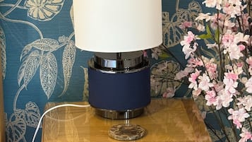 A bedside table with a lamp, a drawer, and a power cord plugged in.