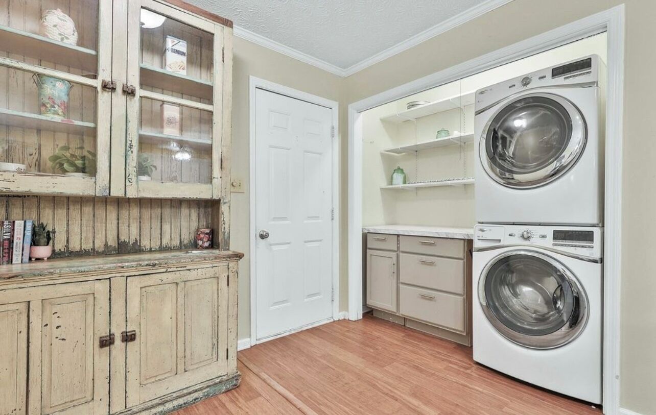 Un cuarto de lavandería con lavadora, un armario con puertas de vidrio y una puerta blanca.