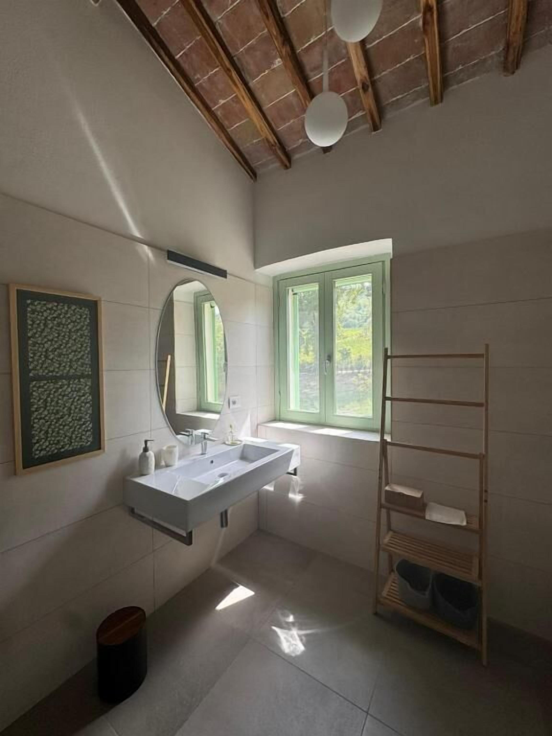 Un baño moderno con un espejo grande, dos lavamanos, una ventana y un estante de madera.