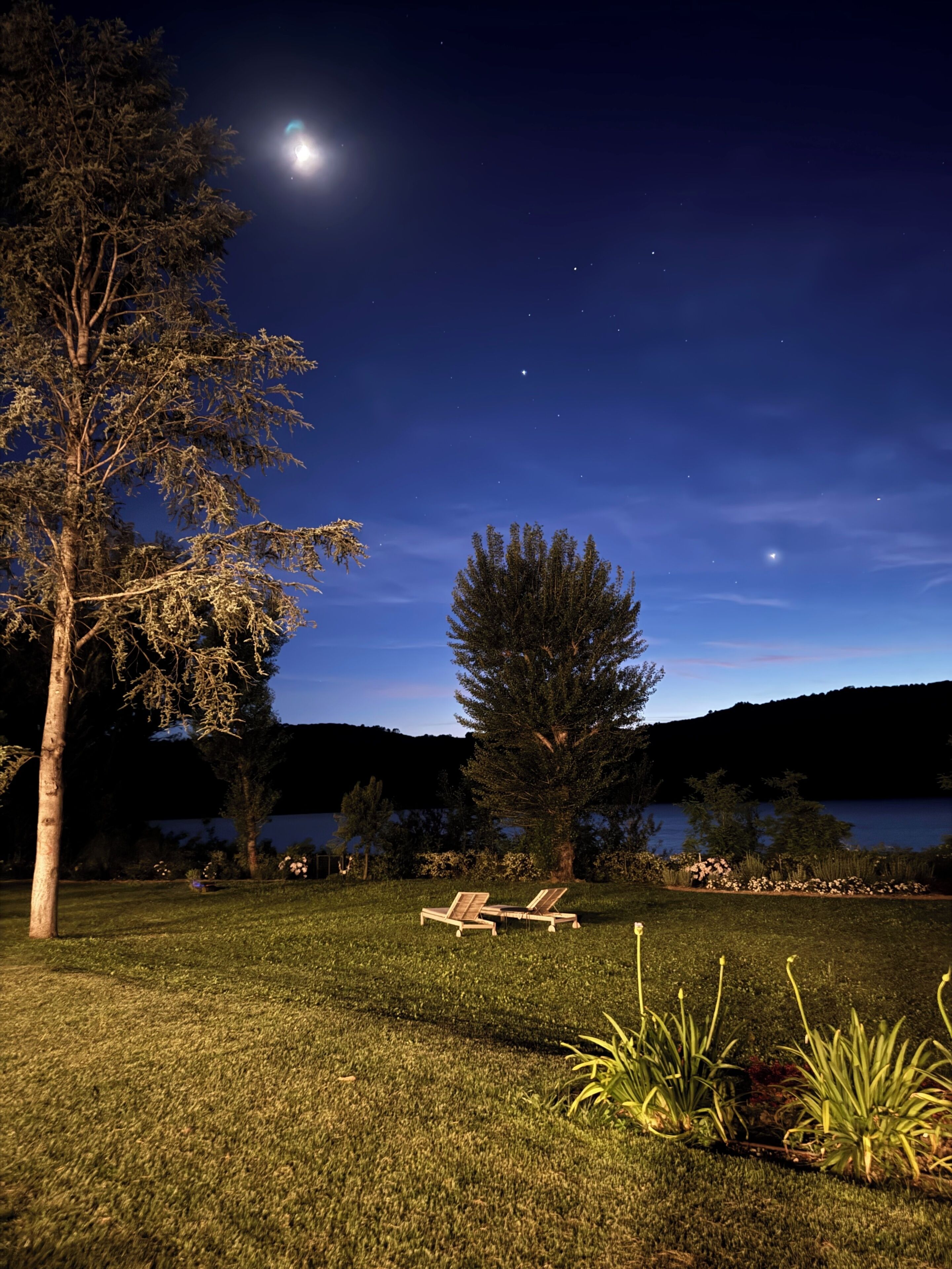Escena nocturna al aire libre bajo un cielo despejado, con una luna llena y un lago al fondo.