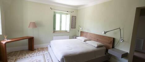 A bedroom with a bed, bedside tables, a bench, a window, and a lamp.