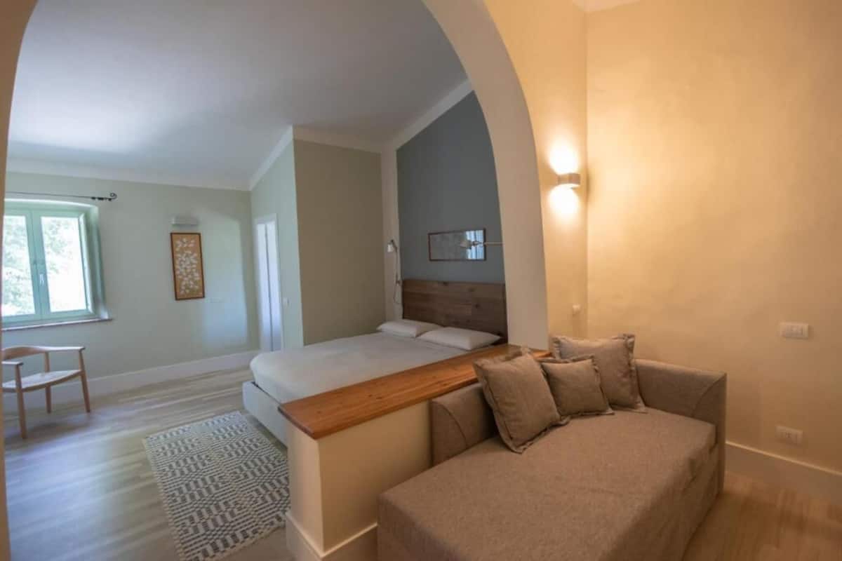 Un dormitorio con cama, sofá, cabecero de madera, luz empotrada en la pared y alfombra estampada.