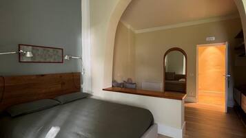 Een slaapkamer met een bed, een houten hoofdeinde, een nachtkastje, een spiegel en een gewelfde deuropening naar een andere kamer.
