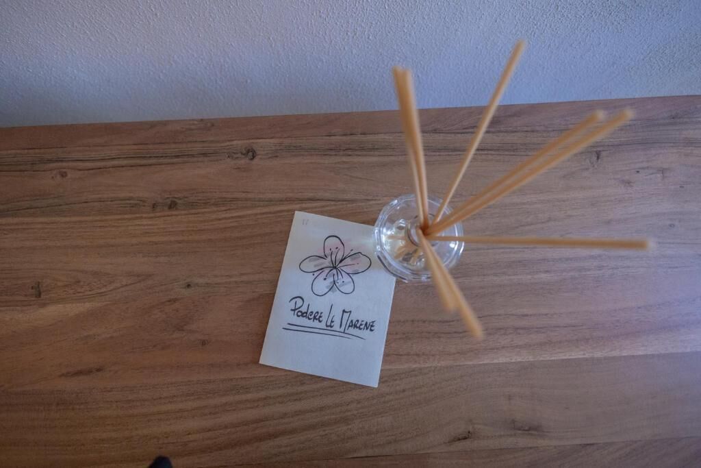 A wooden table with a glass container holding reed sticks and a card with a flower design and text.
