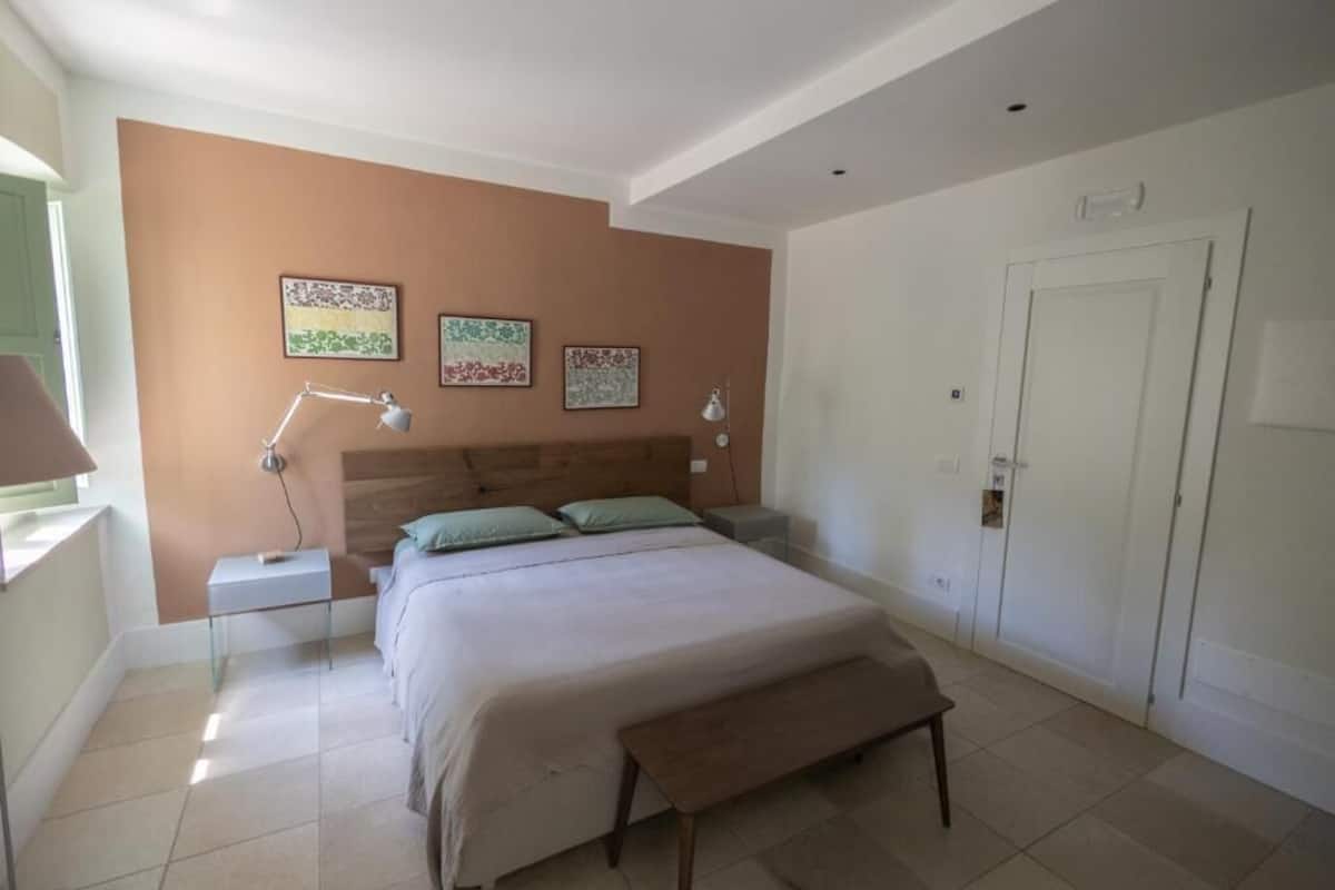 Un dormitorio con cama, mesitas de noche, un banco y una obra de arte en la pared.