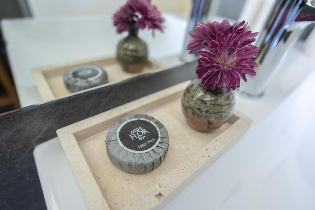A bathroom counter with a soap dispenser, a small vase with a flower, and a mirror reflecting the scene.
