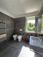 A modern bathroom with a bidet, toilet, and a large bathtub.