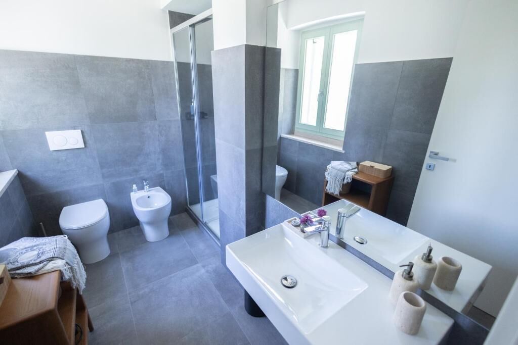 Een moderne badkamer met douche, toilet, bidet en een ruime wastafel met spiegel.