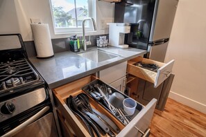 Una cocina con estufa, pileta, cafetera y un cajón con utensilios.