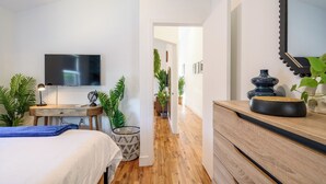 Ein Schlafzimmer mit Bett, Nachttisch, Lampe, Fernseher und Topfpflanzen.