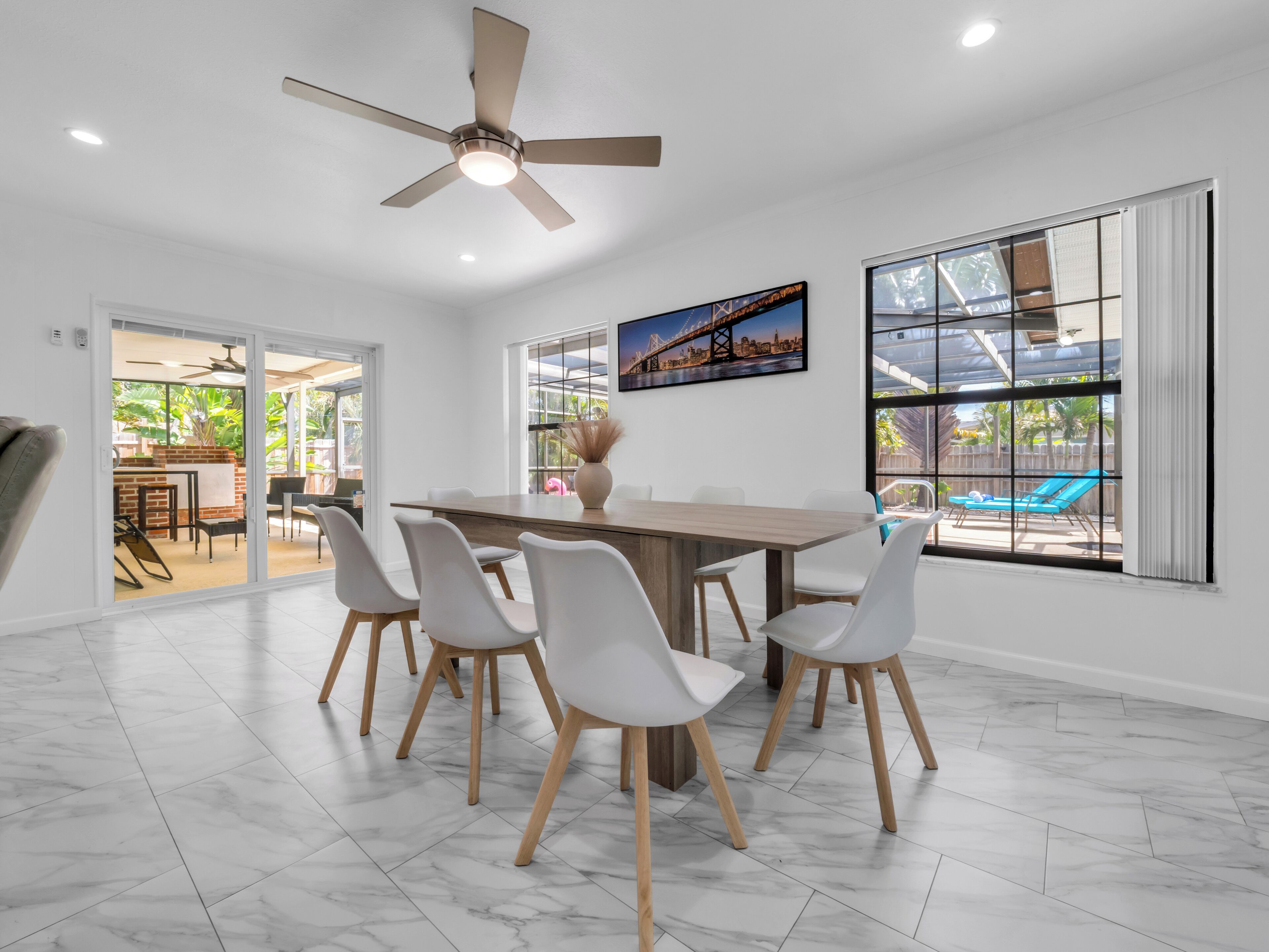 Un espace repas comprenant une table, des chaises, un ventilateur de plafond et de grandes fenêtres.