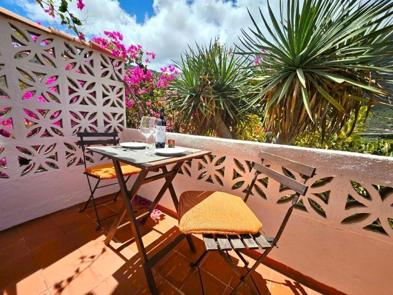 An outdoor patio with a table and chairs, surrounded by a white decorative fence and tropical plants.