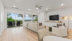 Un salón amplio con un conjunto de sofás, televisión y vistas a una terraza exterior por medio de una puerta corrediza de vidrio.