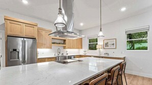 Una cocina moderna con una isla grande, electrodomésticos de acero inoxidable, armarios de madera e iluminación colgante.