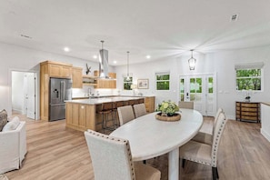 A modern kitchen with a central island, wooden cabinets, and a dining area with a round table and chairs.