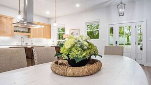 Una cocina moderna con armarios de madera, una mesa de comedor blanca y una gran planta en maceta como centro de mesa.
