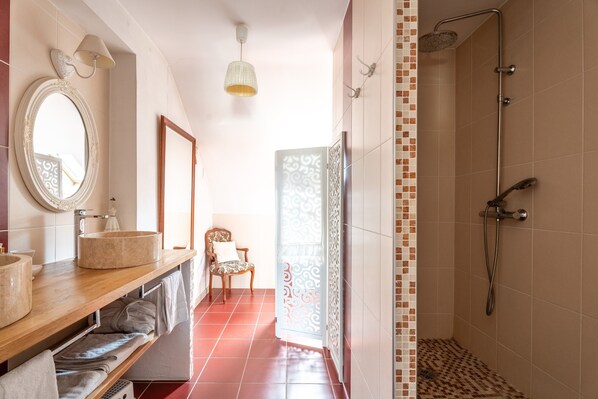 Un baño con ducha, lavamanos, espejo y una silla.
