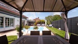 Une terrasse couverte avec une piscine, des chaises longues et une table.