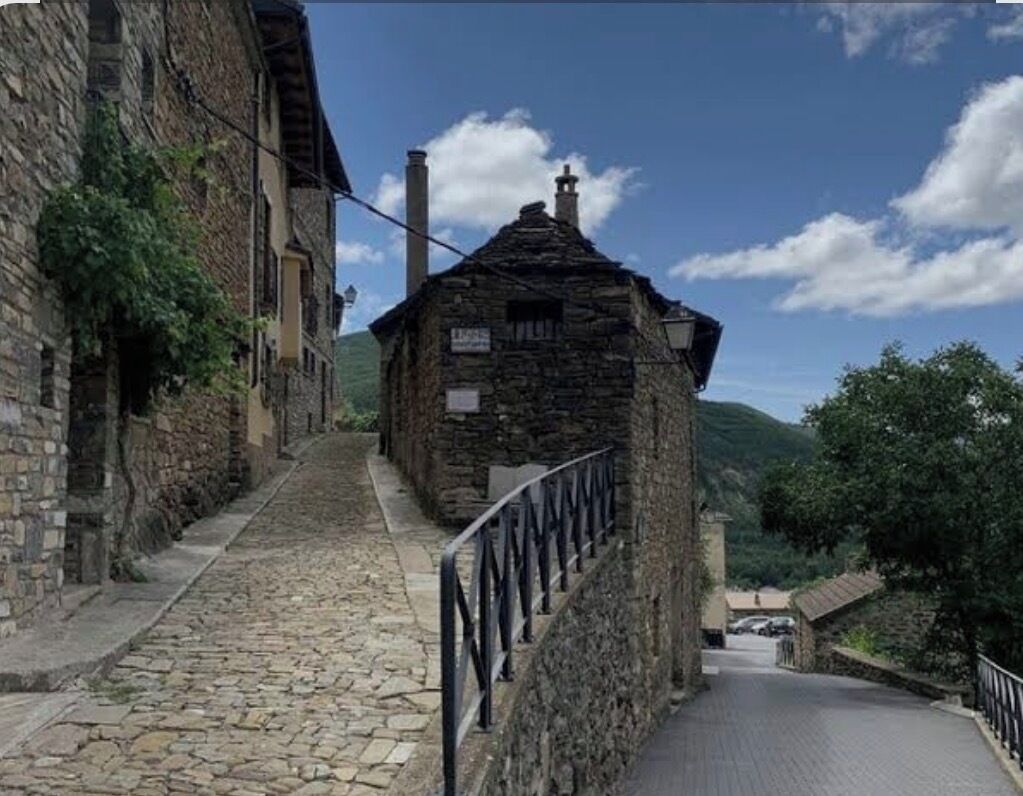 Un bâtiment en pierre avec un escalier menant à une zone pavée, entouré de murs en pierre et de verdure.