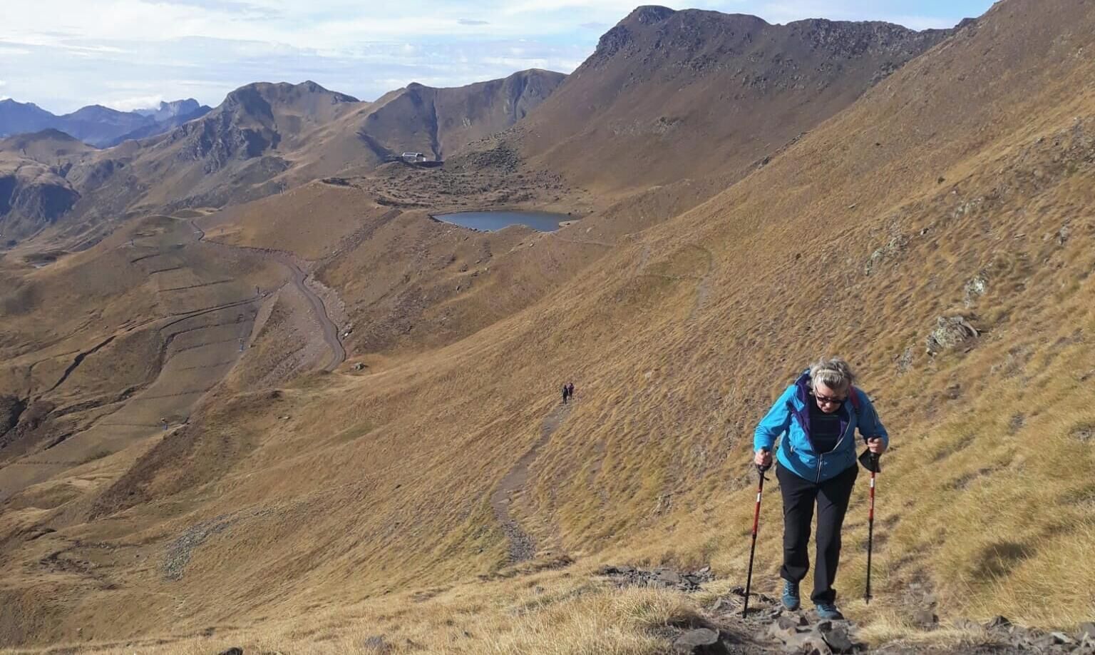 A hiker on a mountain trail with a lake and distant mountains in the background.