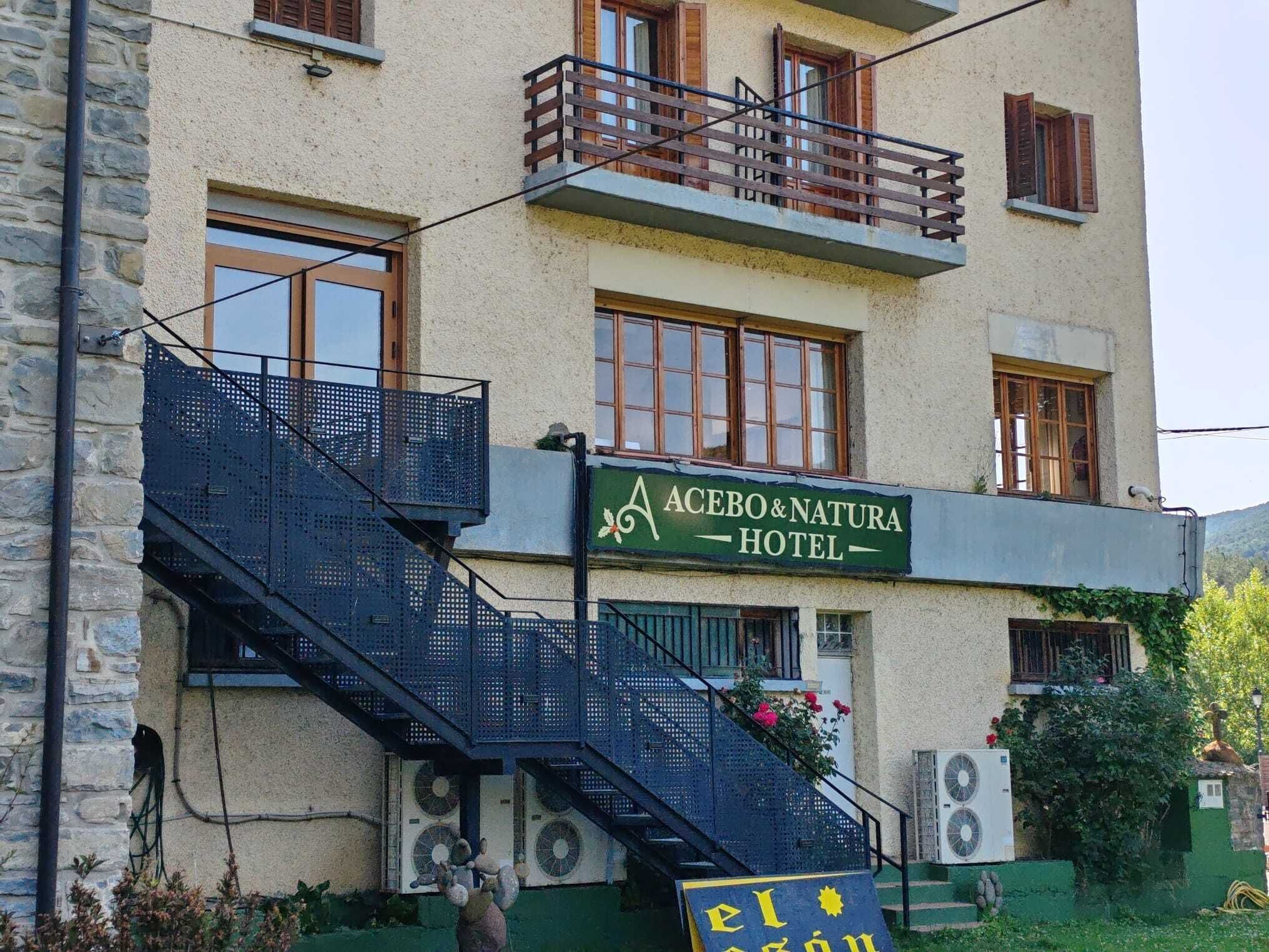Ett hotell med en skylt där det står ”ACEBO & NATURA HOTEL”, en trappa och luftkonditioneringsaggregat.