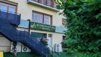 Un hotel con un cartel que dice 'ACEBO & NATURA HOTEL', una escalera que conduce a la entrada y un césped verde al frente.