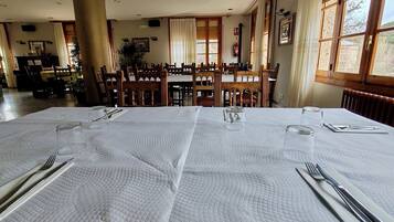 Een eetruimte met een grote tafel gedekt voor vier personen, houten stoelen en uitzicht op de omgeving door grote ramen.
