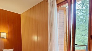 Habitación con dos camas, paredes de madera, una ventana con cortinas y vista a árboles.