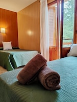 Habitación con dos camas, paredes de madera, una ventana con cortinas y vista a árboles.