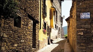 Una estrecha calle adoquinada con edificios de piedra, un cartel que dice 'Calle La Jolesia' y un farol.