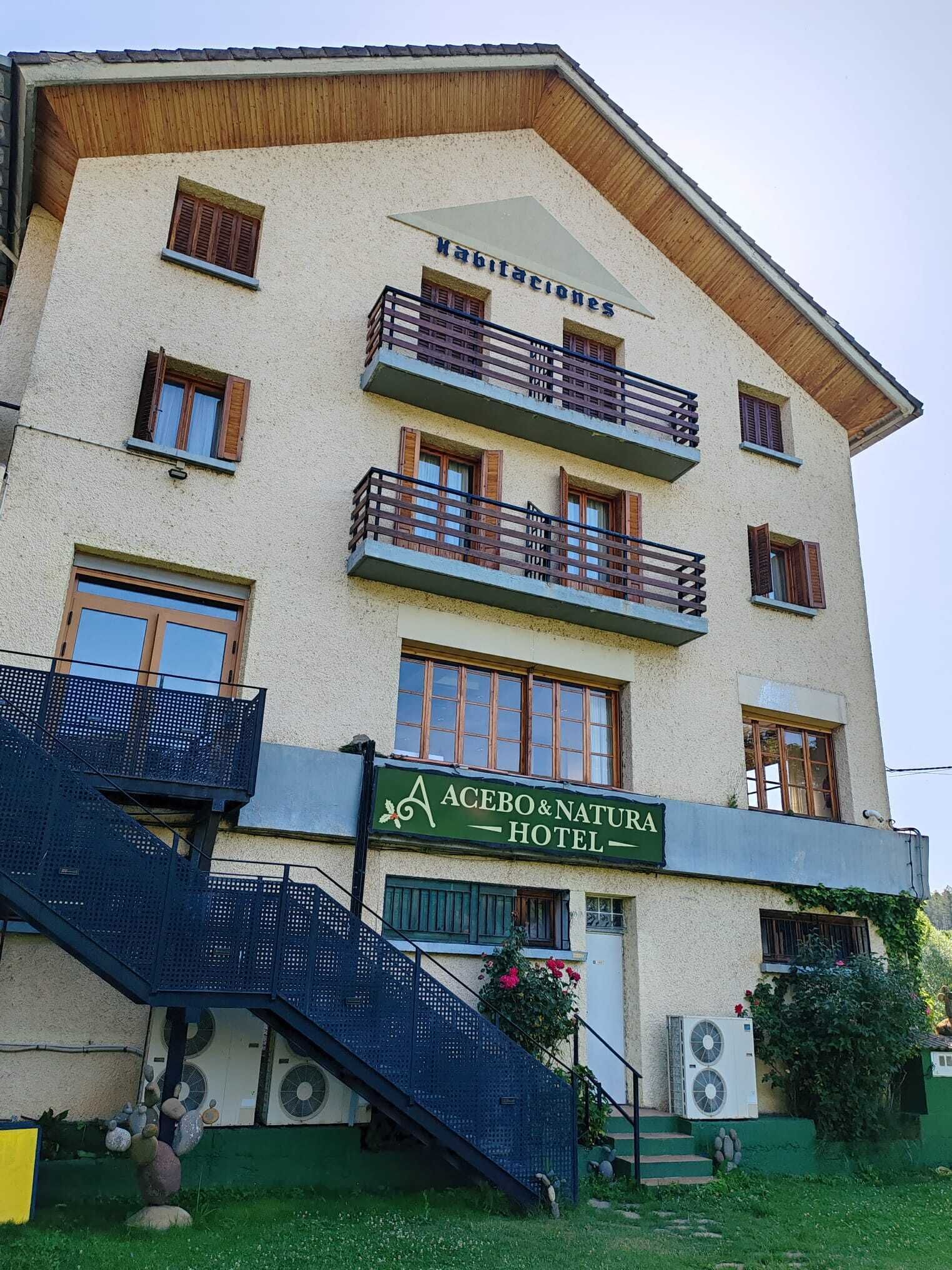A multi-story building with balconies, a sign for 'Acebo & Natura Hotel,' and a staircase leading to the entrance.