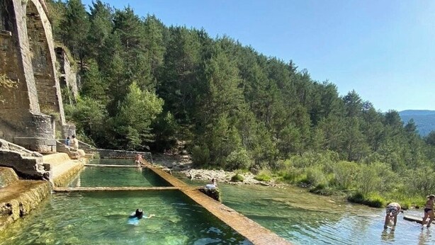 Una piscina cristalina con una estructura de piedra en un lateral, rodeada de árboles.